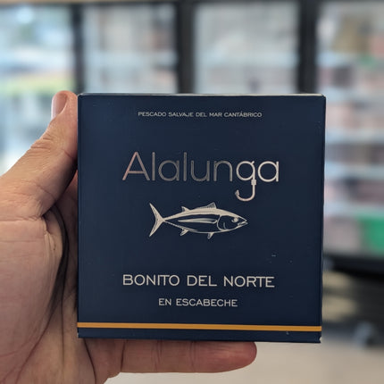 Hand holding a blue box labeled 'Alalunga Bonito del Norte' with a blurred store background.