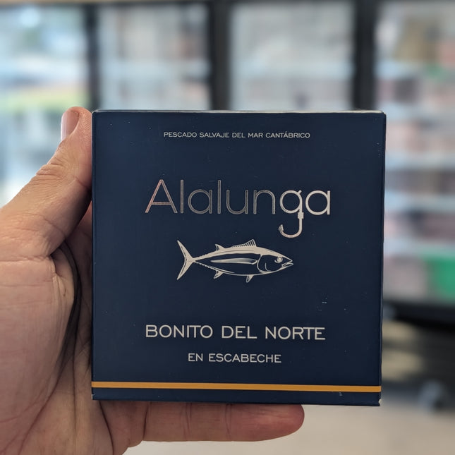 Hand holding a blue box labeled 'Alalunga Bonito del Norte' with a blurred store background.