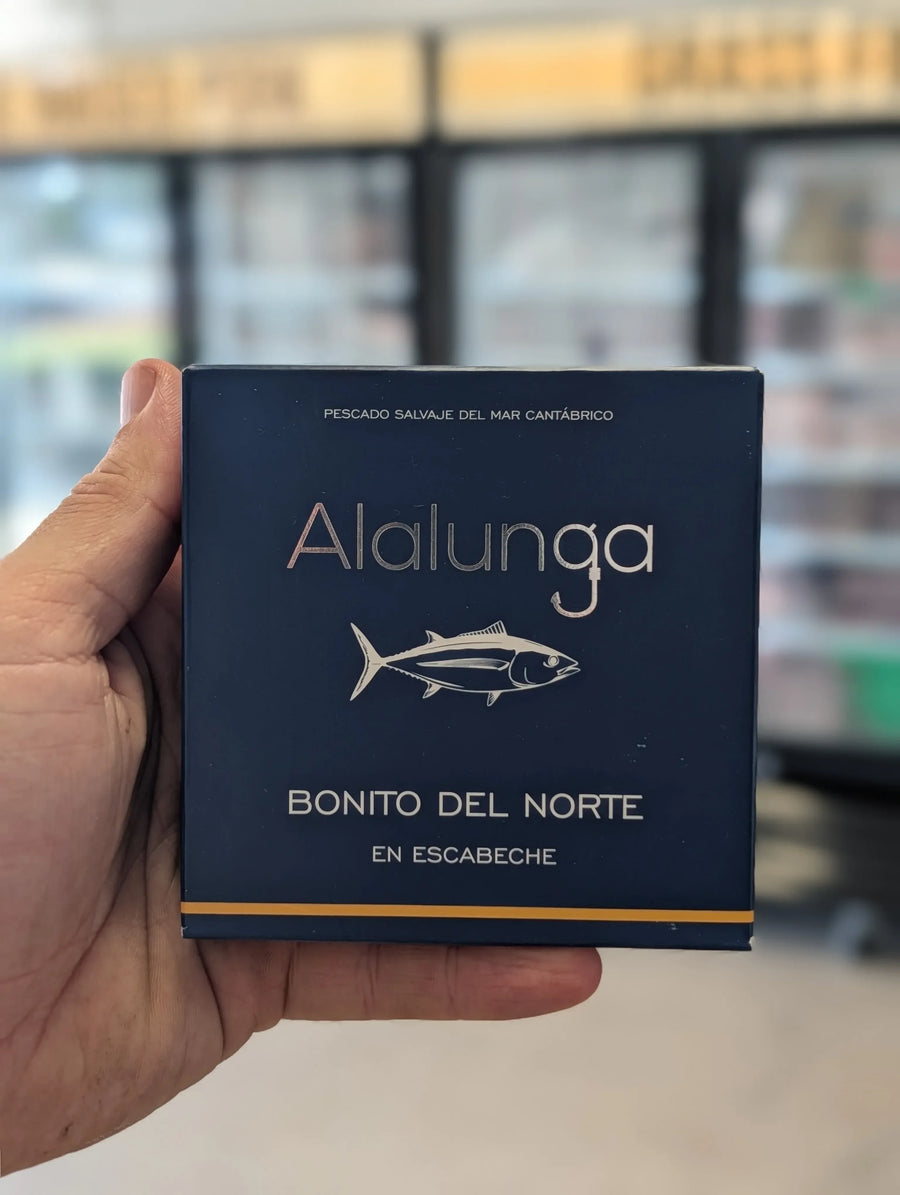 Hand holding a blue box labeled 'Alalunga Bonito del Norte' with a blurred store background. — view 2
