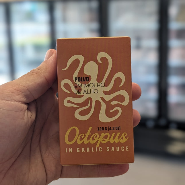 Hand holding a box of 'Octopus in Garlic Sauce' with an octopus logo.