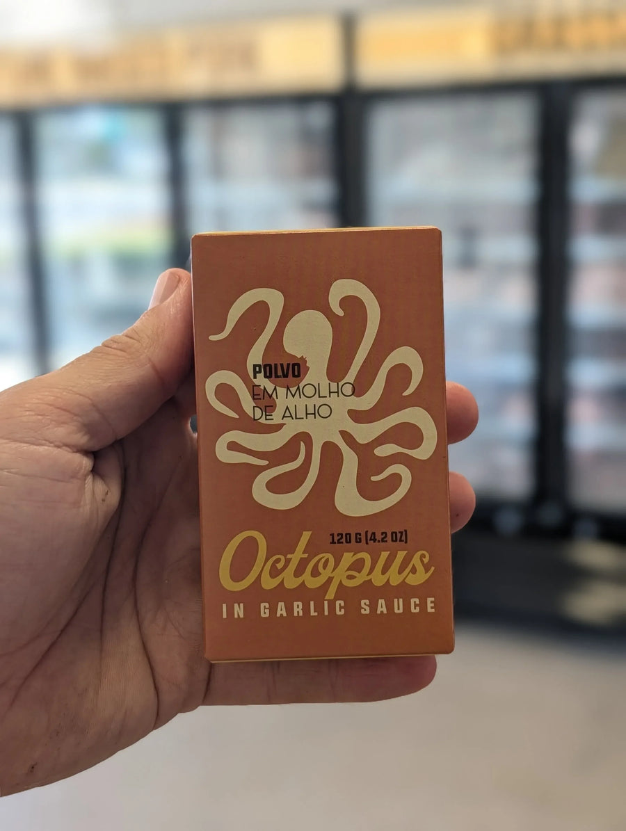 Hand holding a box of 'Octopus in Garlic Sauce' with an octopus logo. — view 2