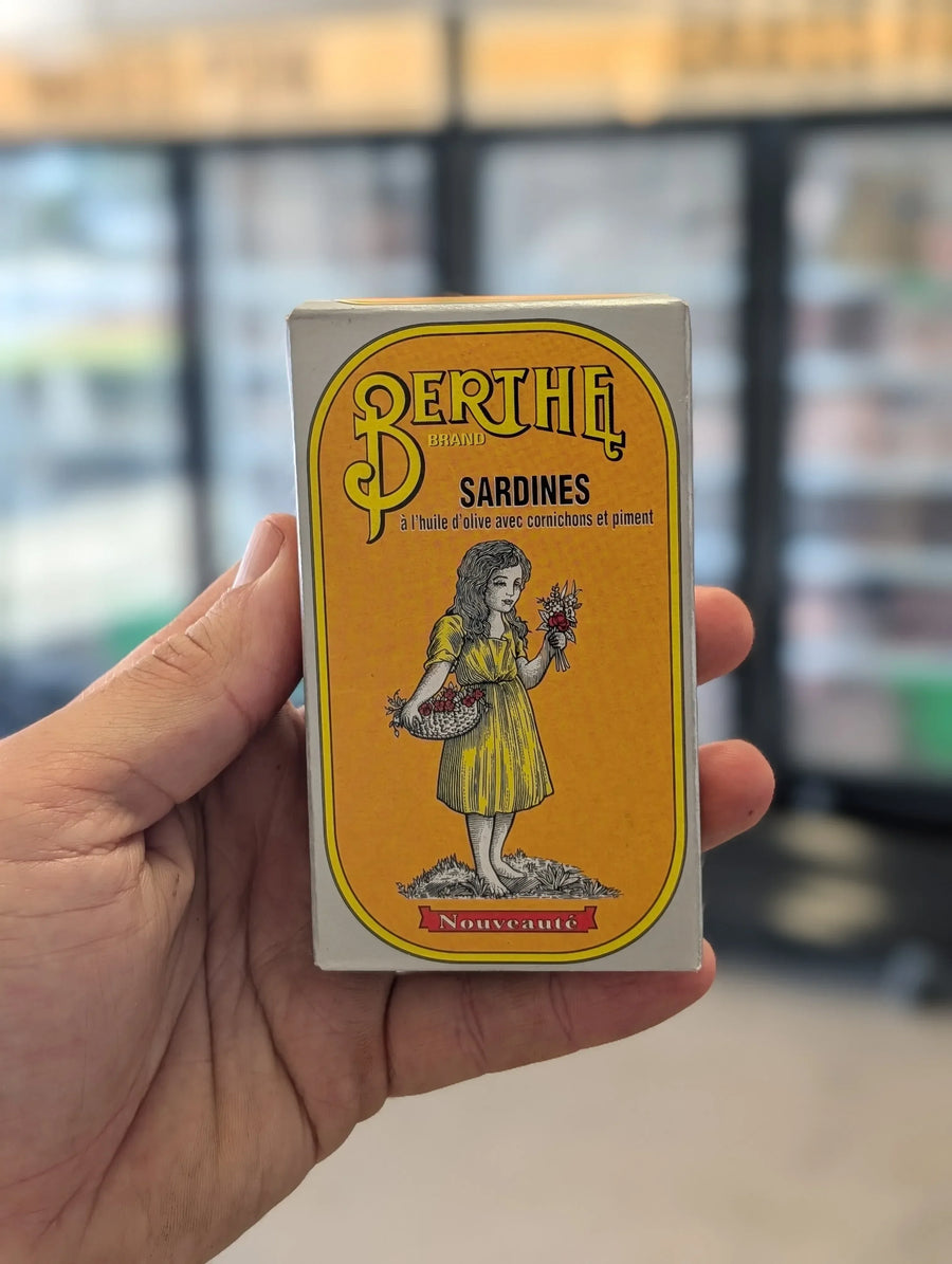 Hand holding a vintage-style Berthe sardine can packaging with a yellow label. — view 2