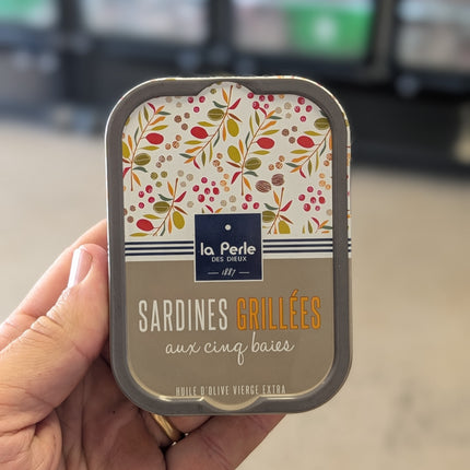 Hand holding a can of 'Sardines Grillées' with floral design on the label.