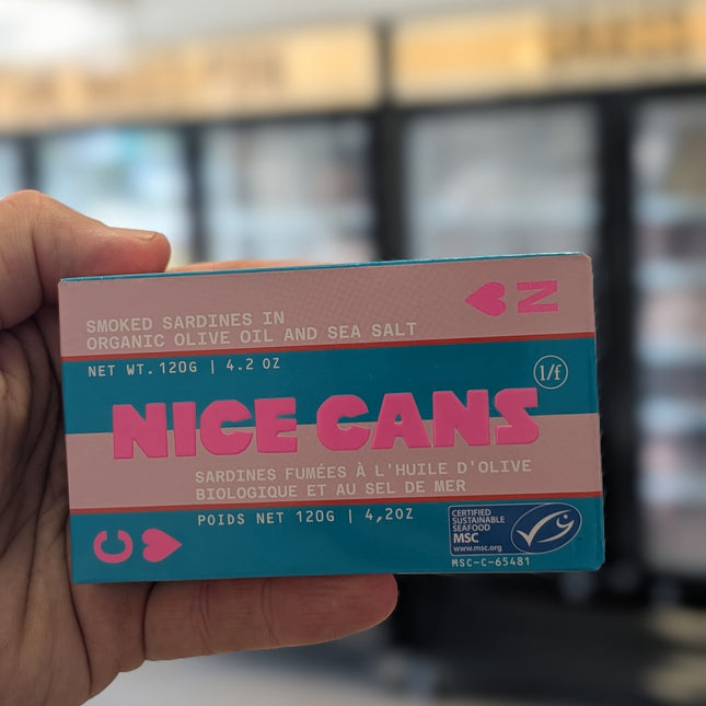 Hand holding a 'Nice Cans' product packaging with a blurred background