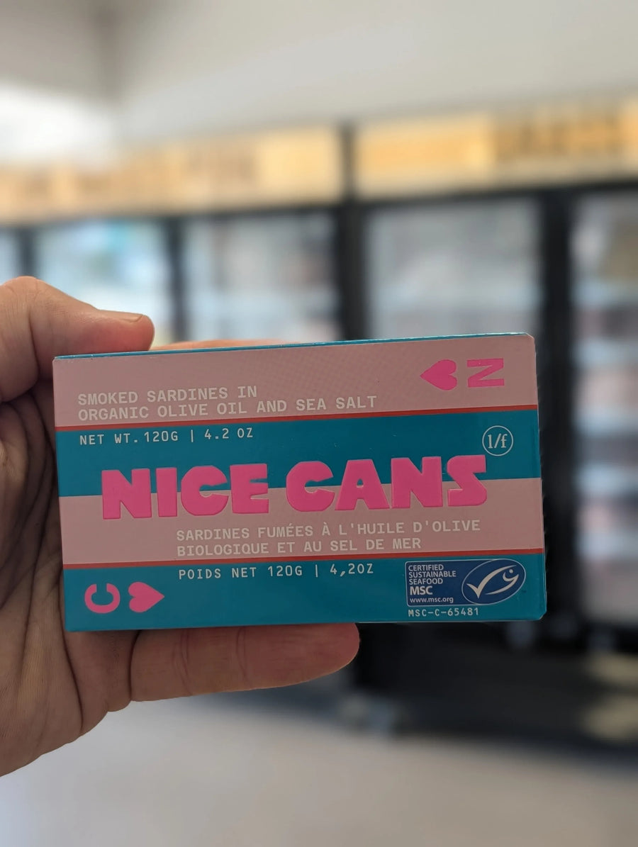 Hand holding a 'Nice Cans' product packaging with a blurred background — view 2