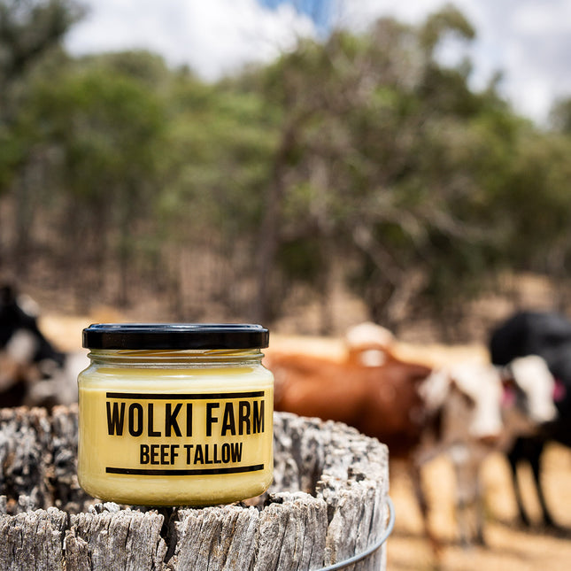 Jar of Wolki Farm beef tallow on a wooden barrel with cows in the background