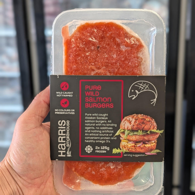 Packaged salmon burgers held in a hand with a blurred background