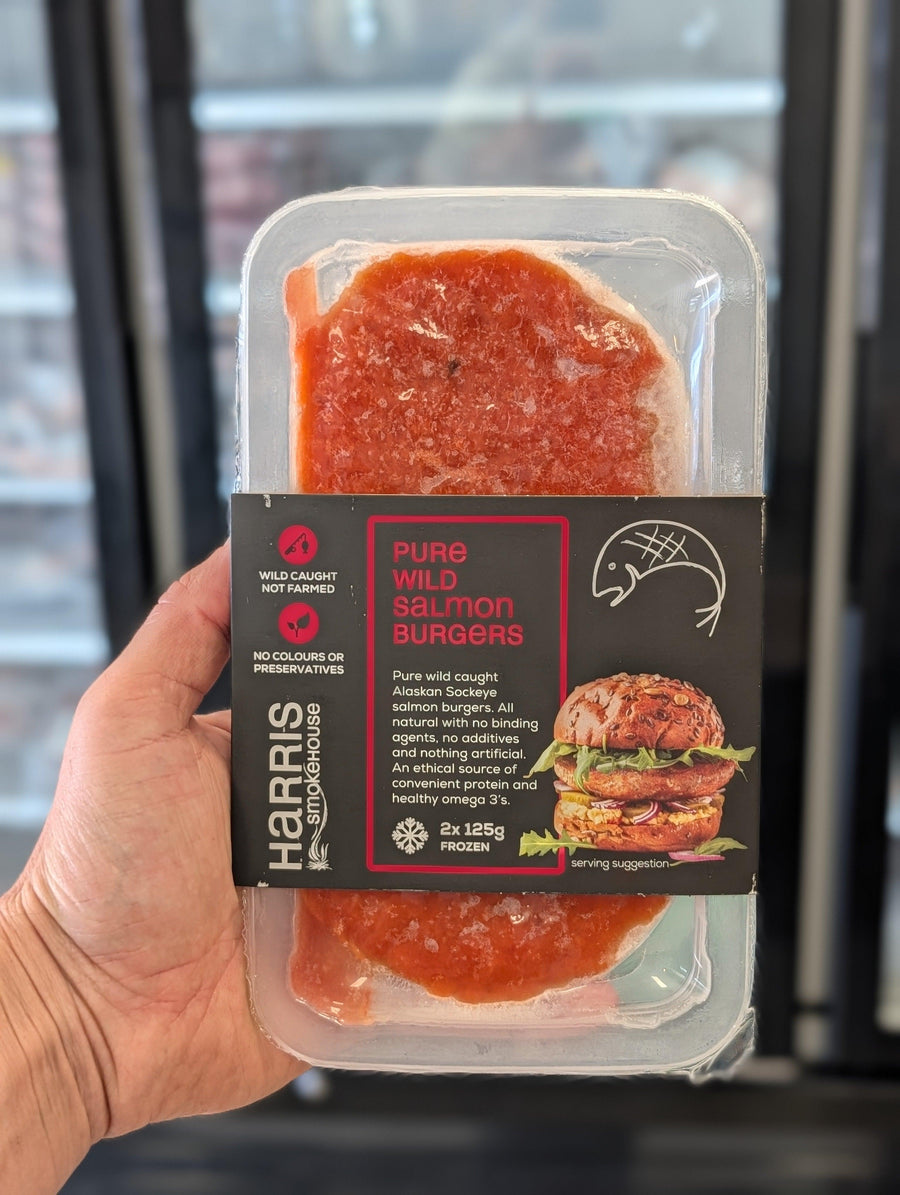 Packaged salmon burgers held in a hand with a blurred background — view 2