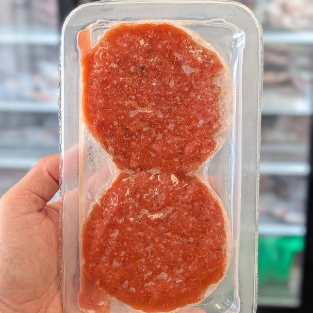 Two round, red meat patties in a clear plastic packaging held by a hand.