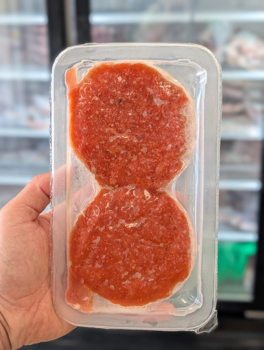 Two round, red meat patties in a clear plastic packaging held by a hand. — view 4