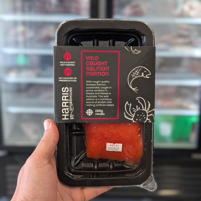 Hand holding a package of wild-caught salmon with 'Harris' branding.