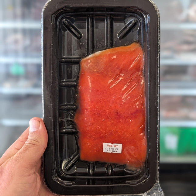 Hand holding a package of raw salmon with a blurred background