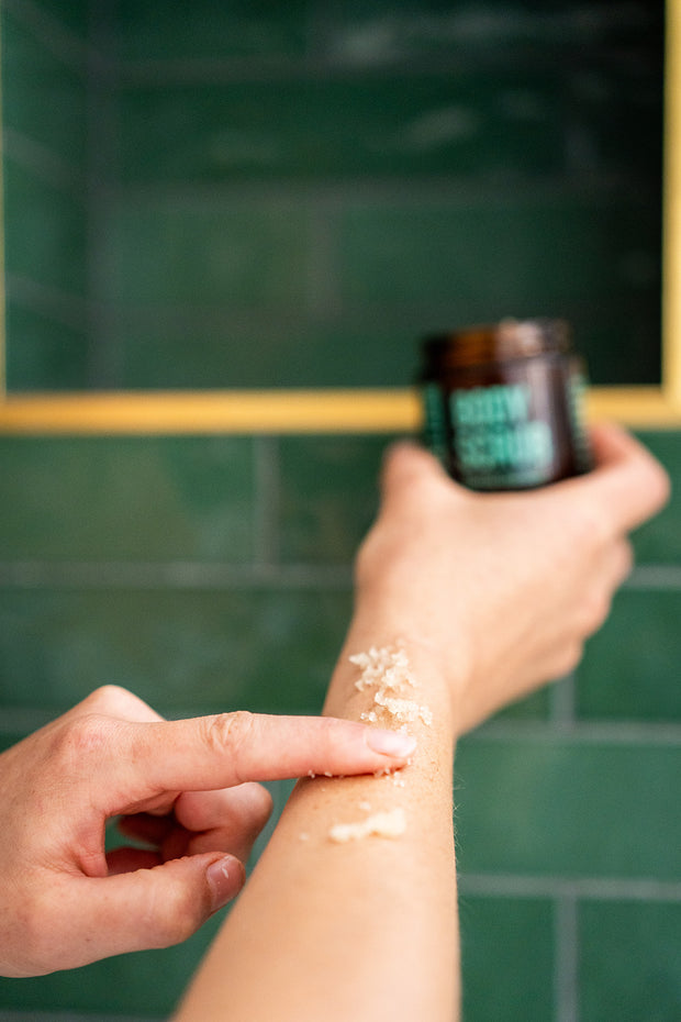 Person applying a product to their arm with a green tiled wall in the background