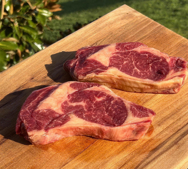 Thick-cut marbled Wolki Farm double aged dairy beef steaks on a timber board in golden farm light