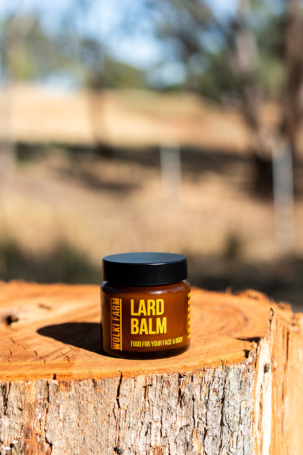 Jar of lard balm on a wooden log with a blurred natural background