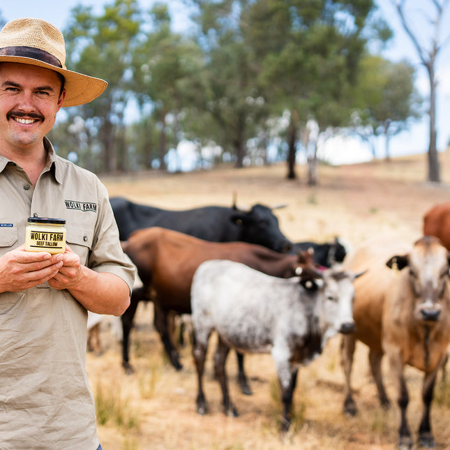 Man holding a cup with cows in the background on a farm